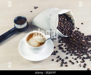 Tazza di caffè, chicchi di caffè tostati e supporto della macchina espresso in una borsa di tela su sfondo scuro Foto Stock