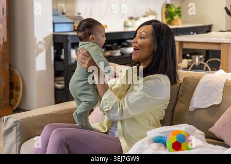 Madre e bambina afroamericana che sorride sul divano beige con onesie verdi Foto Stock