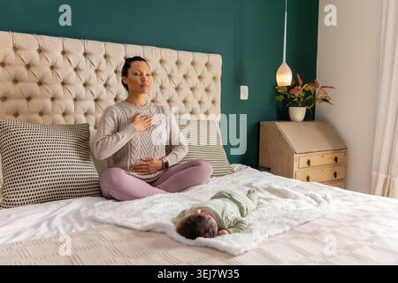 La madre e la figlia della metà degli anni '30 sedevano seduti a gambe incrociate a meditare sul letto con testiera trapuntata Foto Stock