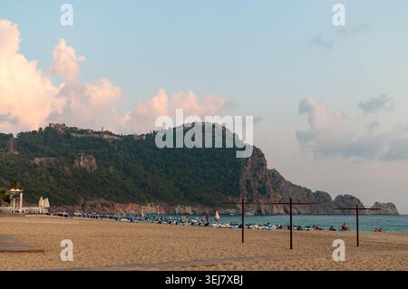 Un'ampia costa sabbiosa della spiaggia di Cleopatra ad Alanya, Turchia, con file di lettini sotto un morbido cielo serale. Foto Stock