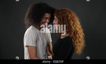 Coppia variegata con capelli ricci che sorridono e toccano la fronte, mostrando amore e connessione Foto Stock