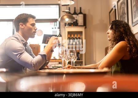 Giovane coppia seduta faccia a faccia durante una conversazione emotiva o seria in un accogliente ristorante. Luce ambiente calda, linguaggio naturale del corpo e au Foto Stock