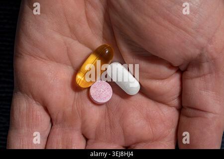 Tre diverse pillole e capsule nella palma umana. Mano che tiene in mano una capsula di gel giallo una compressa bianca e una pillola macchiata rosa che rappresenta la salute quotidiana ro Foto Stock