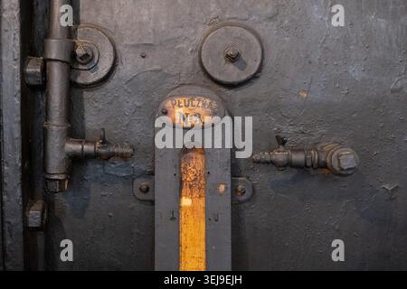Una valvola di controllo industriale manuale con un manico in legno è fissata a un alloggiamento per macchinari pesanti in fabbrica. Foto Stock
