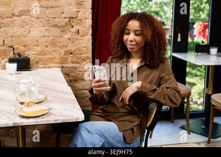La giovane donna si diverte a trascorrere il tempo in un elegante bar, a controllare i messaggi e ad assaporare il dessert. Foto Stock