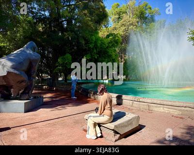 Persone accanto a una grande scultura pubblica accanto alla fontana in Plaza Luis Cabrera, una piazza alberata a Roma Norte, città del Messico, Messico Foto Stock