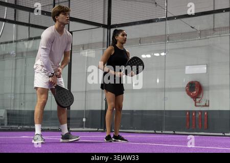 Due giocatori in piedi su un campo viola che reggono pagaie rotonde, indossando abbigliamento sportivo da pareti di vetro Foto Stock