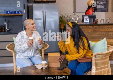 Diverse amiche femminili sedute l'una di fronte all'altra al tavolo del caffè, tenendo caffè e pasticceria Foto Stock