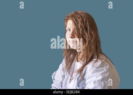 Giovane donna caucasica con lunghi capelli marroni in camicia a righe blu rivolta lateralmente Foto Stock