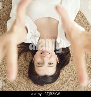 Giovane donna caucasica sdraiata su un tappeto tessuto sorridente con braccia allungate Foto Stock