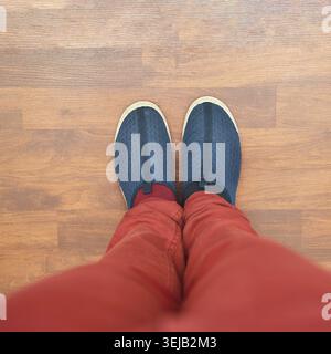 Vista dall'alto dei pantaloni rossi e delle scarpe blu sul pavimento in legno Foto Stock