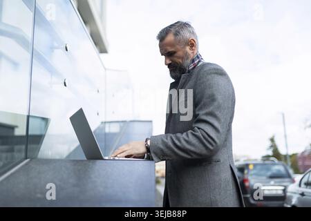 Uomo d'affari dai capelli grigi che lavora su un computer portatile esterno Foto Stock