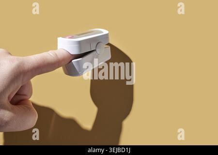 Dito caucasico per adulti che utilizza pulsossimetro su sfondo marrone per il monitoraggio sanitario Foto Stock