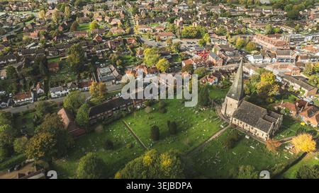 Una prospettiva elevata mette in mostra un affascinante villaggio annidato tra alberi che mostra un vivace fogliame autunnale, centrato intorno a un'antica chiesa e ad essa Foto Stock