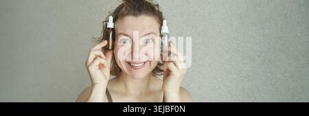 Donna caucasica sorridente che tiene flaconi di siero su sfondo chiaro Foto Stock