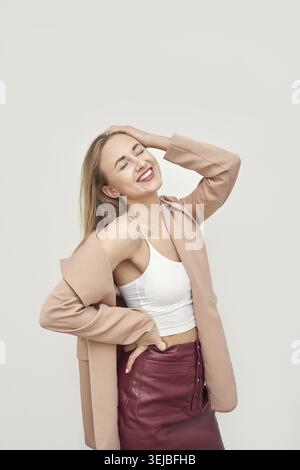 Donna caucasica con bagliore rosa e gonna rossa che si posa felicemente su sfondo neutro Foto Stock