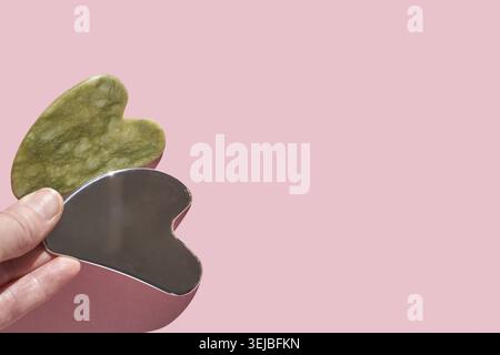 Utensili Gua Sha: Giada verde e pietra massaggiante in acciaio inossidabile su un morbido sfondo rosa per la cura del viso Foto Stock