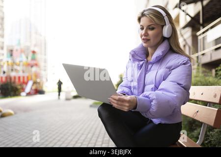 Donna matura con le cuffie che lavora su un notebook all'aperto Foto Stock