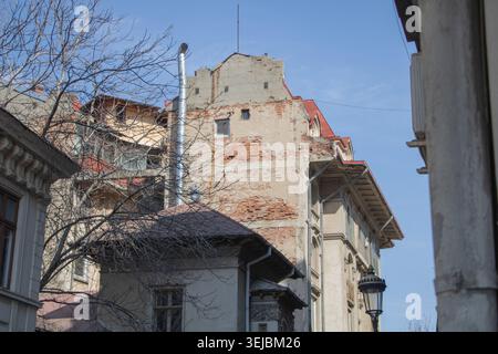 Antico edificio residenziale urbano con pareti in mattoni a vista e facciata deteriorata circondato da architettura storica a Bucarest. Foto Stock