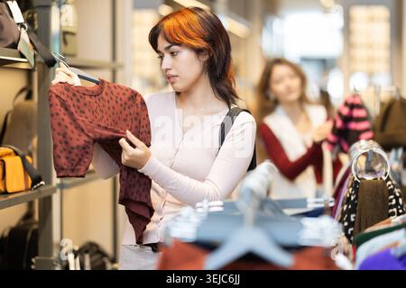 Una giovane donna sceglie un maglione nella boutique di abbigliamento Foto Stock