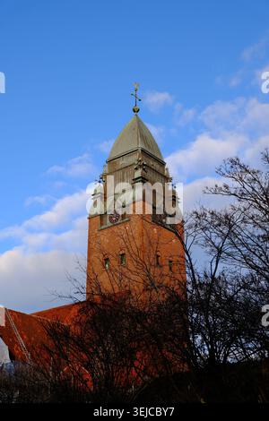 Gothenburg, Svezia - 24 novembre 2025: Colpo a basso angolo della guglia torreggiante della chiesa di Masthugget dietro i rami di alberi sotto un cielo blu a Gothenburg Foto Stock