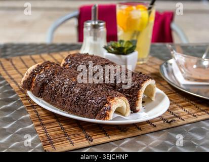 Due tortine a camino al cioccolato Kurtoskalacs con granella di cioccolato servite su un piatto bianco con limonata fresca su un tavolo di un caffè a Budapest, Ungheria Foto Stock