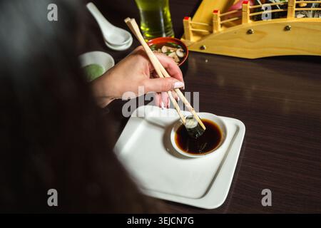 Donna che immerge il sushi Roll Maki in salsa di soia utilizzando bastoncini di legno nel ristorante Foto Stock