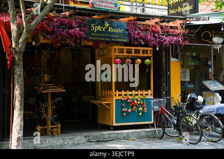 HOI AN, VIETNAM, 19 APRILE 2026 entrata accogliente di un ristorante indiano decorato con fiori e lanterne accanto alle biciclette sulla strada Foto Stock