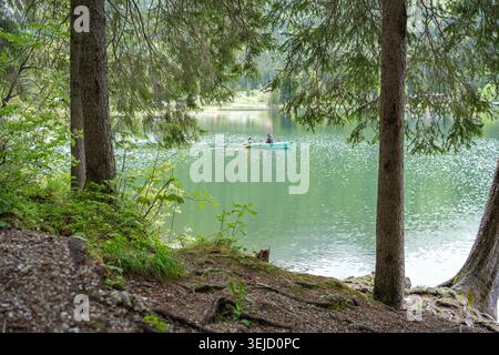 Una vista panoramica di una singola piccola barca a remi che galleggia sulle calme acque verde smeraldo di un lago forestale. Splendido paesaggio alpino selvaggio incorniciato da Foto Stock