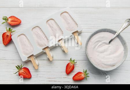 Lo yogurt alla fragola si prepara in muffa con frutti di bosco freschi e cremoso yogurt su un tavolo di legno Foto Stock