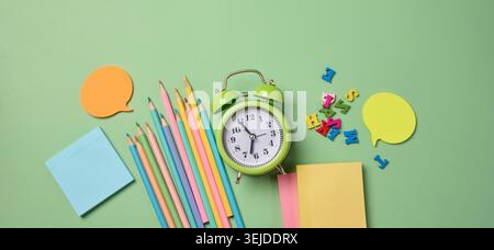 Cancelleria disposta su sfondo verde. Matite multicolore , sveglia, note adesive e lettere di legno, preparazione per la s Foto Stock