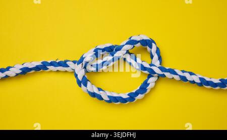 Spesso corda blu legata a un nodo su sfondo giallo Foto Stock