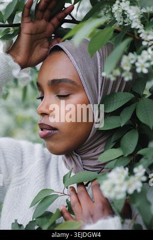 Giovane donna musulmana pacifica in hijab circondata dalla fioritura primaverile Foto Stock