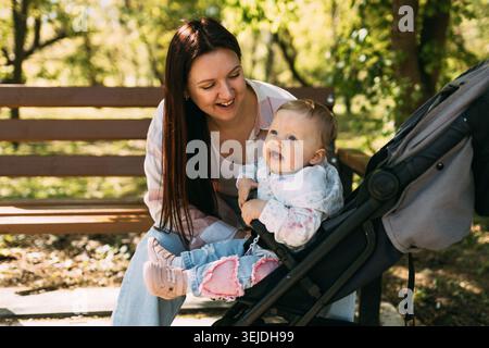 Mamma sorridente che passa il tempo con il bambino nel passeggino del parco soleggiato Foto Stock