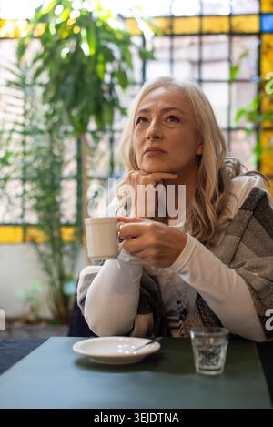 Donna matura che tiene in mano una tazza di caffè con un'illuminazione soffusa Foto Stock