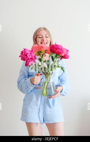 Bella donna in abito color pastello che posa con fiori freschi, ritratto di stile moderno con romantica atmosfera primaverile. Foto Stock