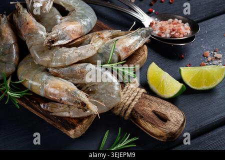 Gamberetti freschi, crudi, gamberetti di tigre vannamei, su un tagliere di legno, con fette di lime e condimenti, Foto Stock