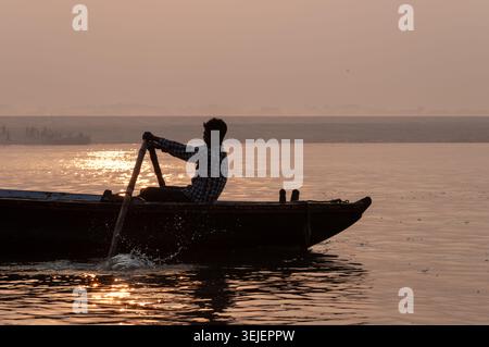 Silhouette di un barcaiolo che canta una tradizionale barca di legno all'alba sul Gange, Varanasi, Uttar Pradesh, India. Foto Stock