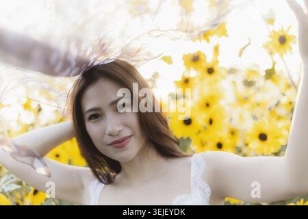 Felice donna asiatica serena che gode della luce del sole estiva nel campo giallo di girasole. Bella giovane modella ritratto all'aperto in natura con bokeh da sogno Foto Stock