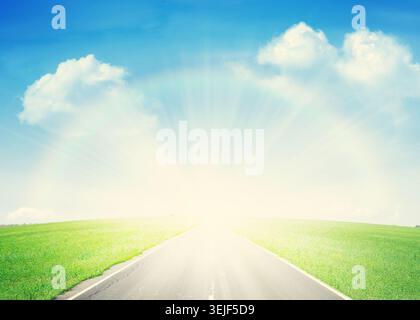 Strada asfaltata attraverso il campo verde e l'arcobaleno Foto Stock