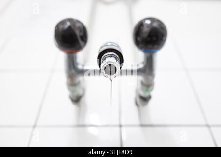 Colpo ad angolo basso di un rubinetto per bucato cromato con manici rotondi neri e un flusso sottile di acqua corrente. Primo piano, ripresa ad angolo basso, niente persone Foto Stock