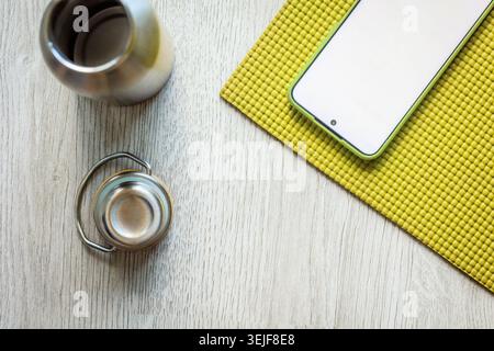 Home yoga Flat con mockup per smartphone, tappetino verde e bottiglia d'acqua riutilizzabile su pavimento in legno chiaro, benessere tranquillo e fitness online Foto Stock