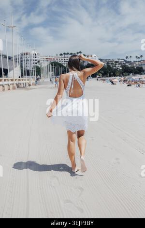 Una donna in abito bianco cammina a piedi nudi sulla spiaggia di sabbia Foto Stock