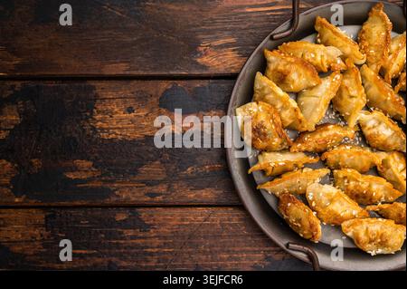 Gnocchi di mandu fritti croccanti con salsa di sesamo su fondo di legno. Adesivi fritti d'oro in una piastra di metallo rustica Foto Stock