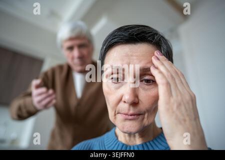Triste infelice donna matura che sopporta aggressione verbale da marito nevrotico in stress emotivo Foto Stock