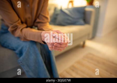 Donna nervosa irriconoscibile siede sul divano con le braccia strettamente incrociate durante la terapia di consulenza Foto Stock