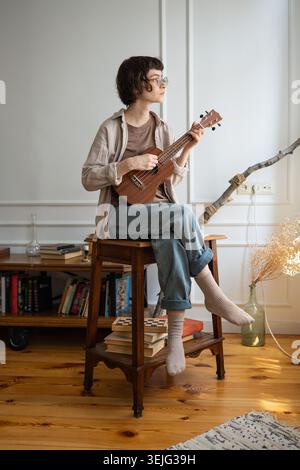 Giovane donna creativa che suona musica con la chitarra acustica ukulele e si gode la musica a casa durante il fine settimana. Foto Stock
