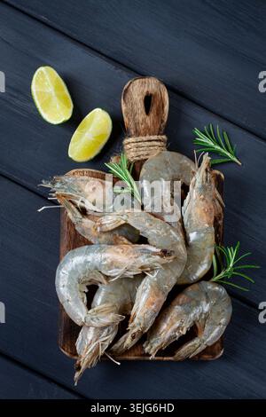 Gamberetti freschi, crudi, gamberetti di tigre vannamei, su un tagliere di legno, con fette di lime e condimenti, Foto Stock