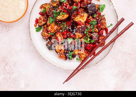 Melanzane fritte, stile cinese, in salsa dolce e acida, con pepe e semi di sesamo. su un piatto bianco, Foto Stock
