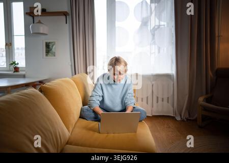 Donna d'affari di mezza età, concentrata e rilassata, seduta comodamente su un comodo divano, che lavora con un computer portatile. Foto Stock